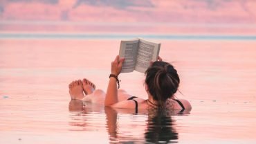 Tourist effortlessly floating while reading a book in the mineral-rich waters of the Dead Sea, Jordan