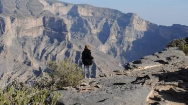 Woman admiring dramatic Jebel Shams Grand Canyon views in Oman, showcasing breathtaking mountain landscape.