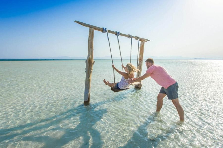 Romantic photo of a couple enjoying the famous water swing in the shallow sea at Orange Bay, Hurghada