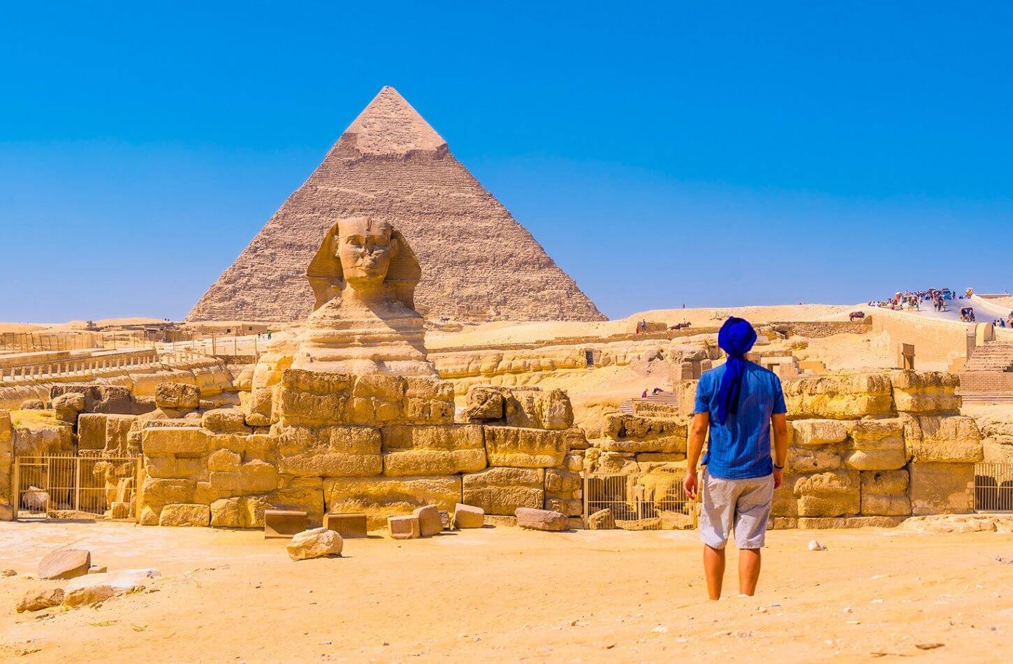 traveler standing before the Great Sphinx with the Pyramids of Giza rising in the background under a clear sky.