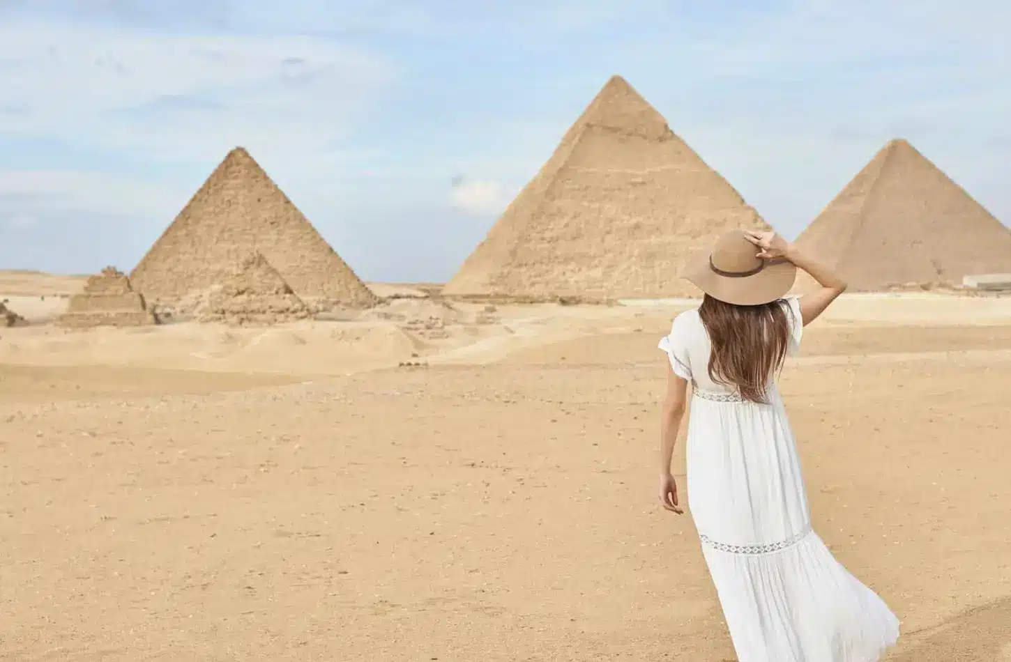 A woman in a sun hat standing in the desert facing the Great Pyramids of Giza, representing how to plan an Egypt tour on a budget.