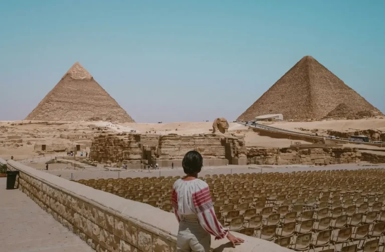 Female traveler dressed in modest attire admiring the Giza Pyramids and Sphinx, following cultural etiquette in Egypt.