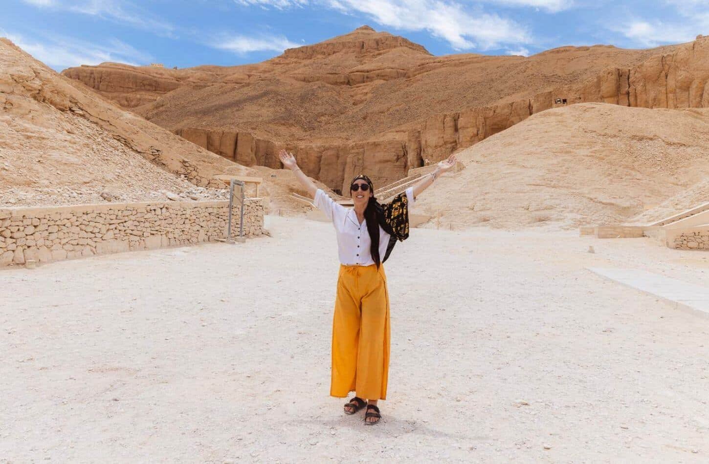 A woman stands in the Valley of the Kings, Luxor, surrounded by desert mountains and limestone cliffs.