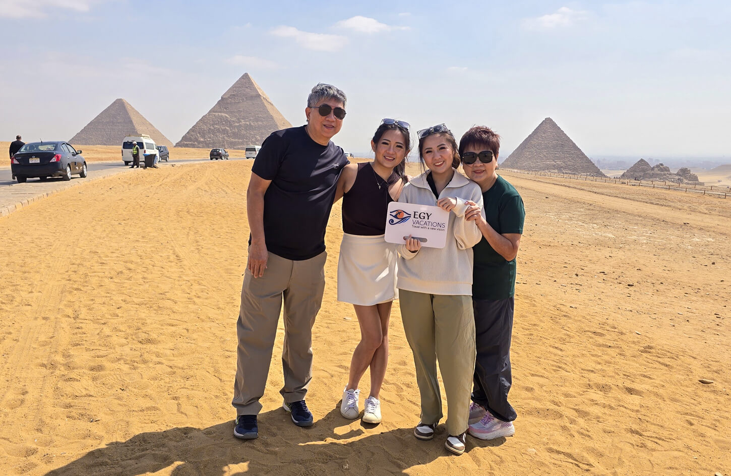 Family exploring Giza pyramids in Cairo, Egypt. Their sign reads: "Egy Vacations, Travel with a new vision." Egypt tours.