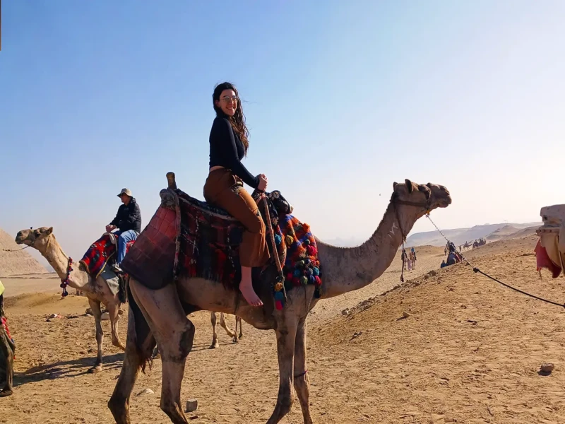 A woman riding a camel through the vast desert landscape of Egypt, showcasing the region's welcoming atmosphere.