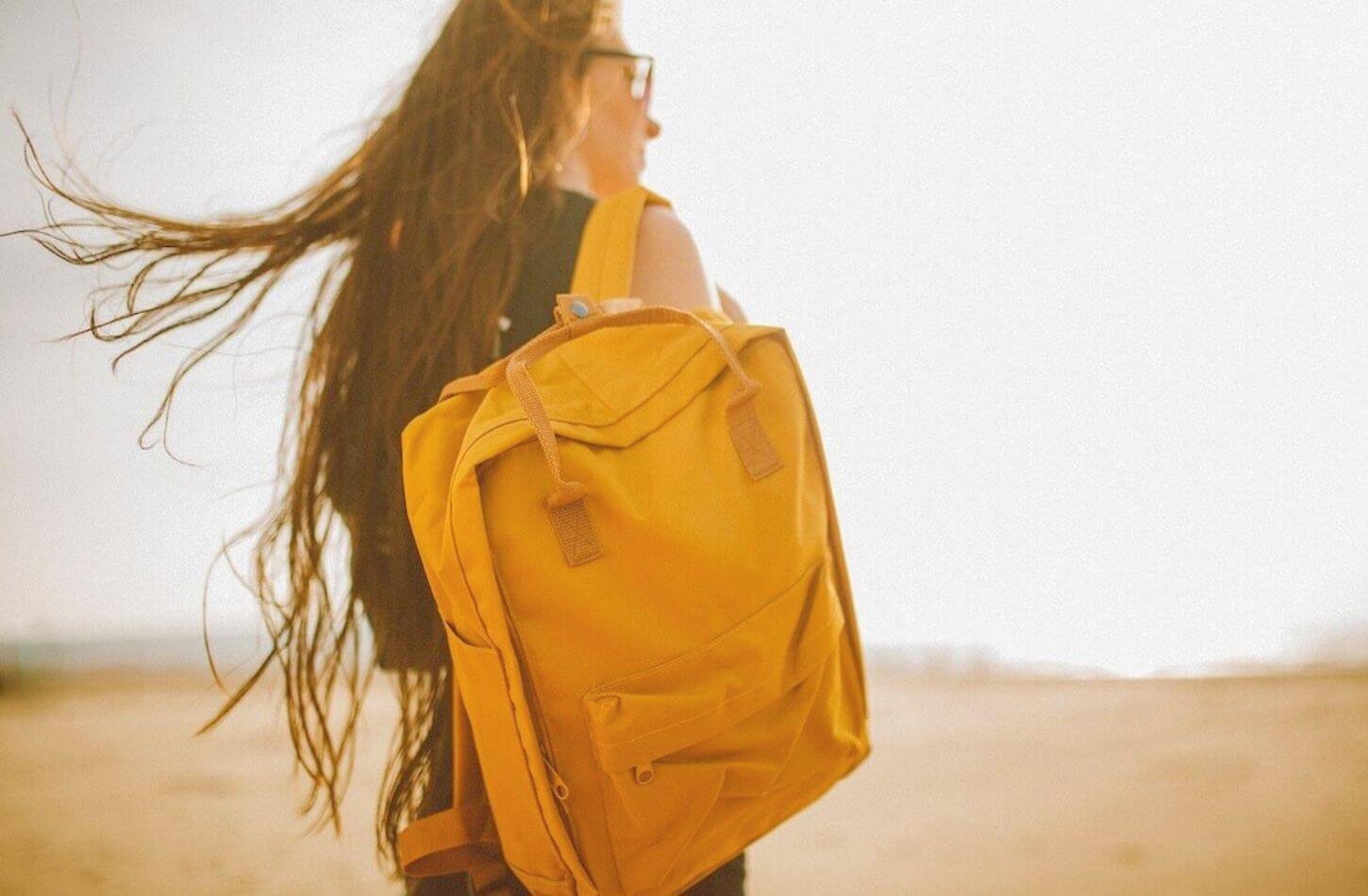 woman wearing yellow backpack walking sand