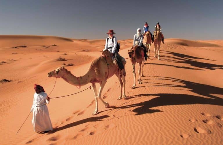 a great shot of some visitors riding camels at wahiba sands in oman