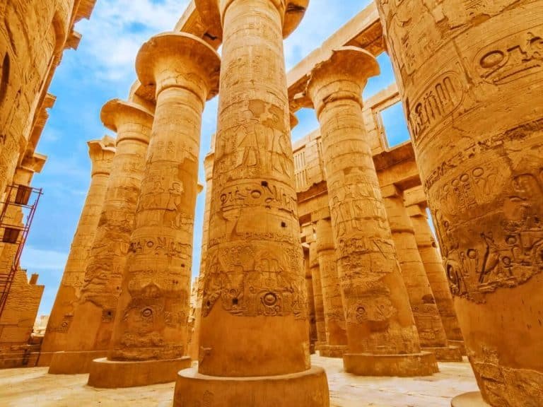 an upclose shot inside karnak temples hypostyle hall towering sandstone columns are covered in intricate hieroglyphs