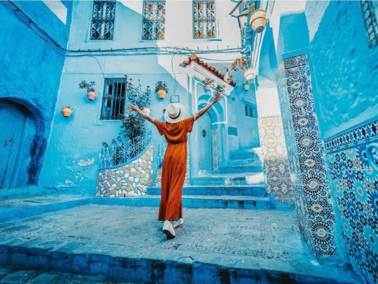 a woman in an orange dress walks joyfully through the vibrant bluepainted alleys of chefchaouen