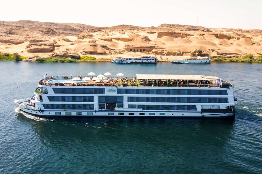 Exterior view of the Amwaj Living Stone ship sailing the Nile River against a striking desert landscape