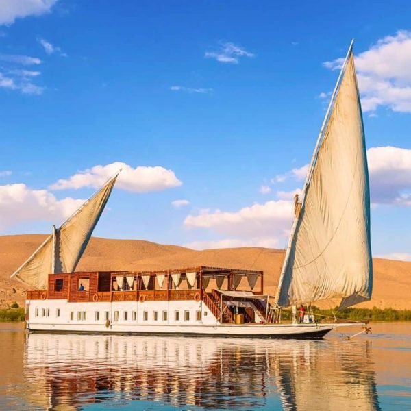 Traditional sailing boat for Dahabiya Nile Cruises sailing past desert hills in Egypt.