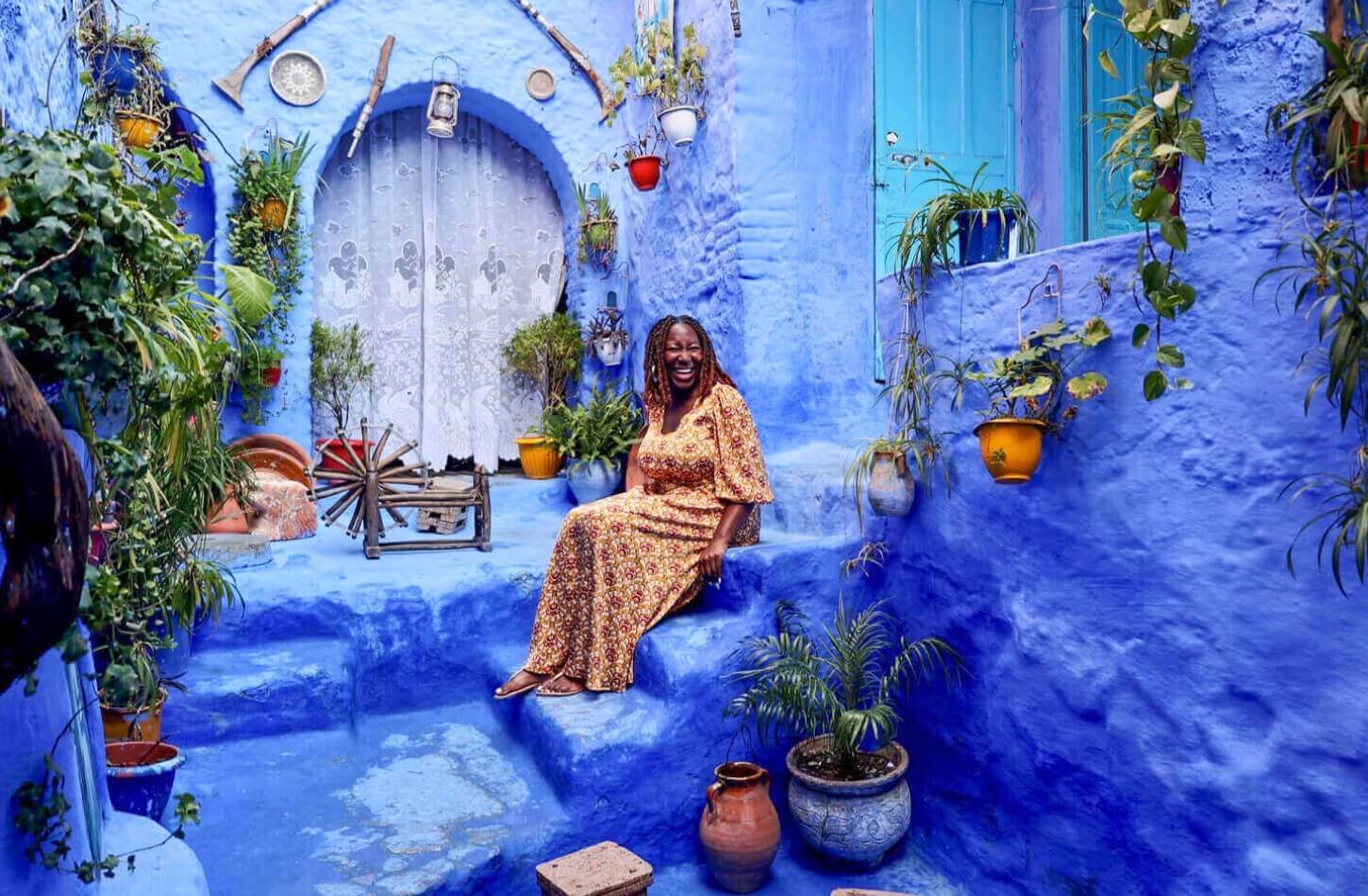 a woman sitting in the bluepainted streets of chefchaouen morocco smiling amid potted plants capturing the charm and calm