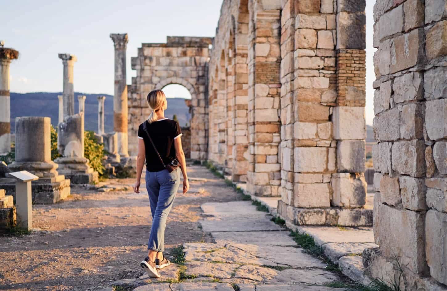 Traveler walking through the well-preserved Roman ruins and columns at the Volubilis archaeological site in Morocco