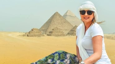 Female tourist visiting the Giza Pyramids in Egypt, sitting on desert sand
