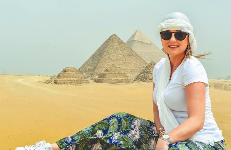 Female tourist visiting the Giza Pyramids in Egypt, sitting on desert sand