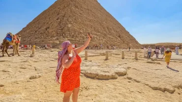 Woman in red dress taking a selfie at the Giza Pyramids Egypt during a sunny desert tour