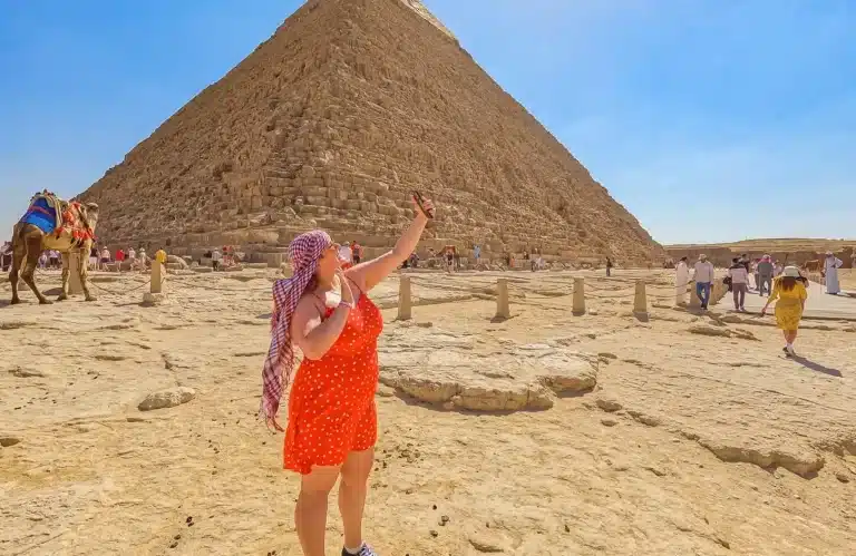 Woman in red dress taking a selfie at the Giza Pyramids Egypt during a sunny desert tour