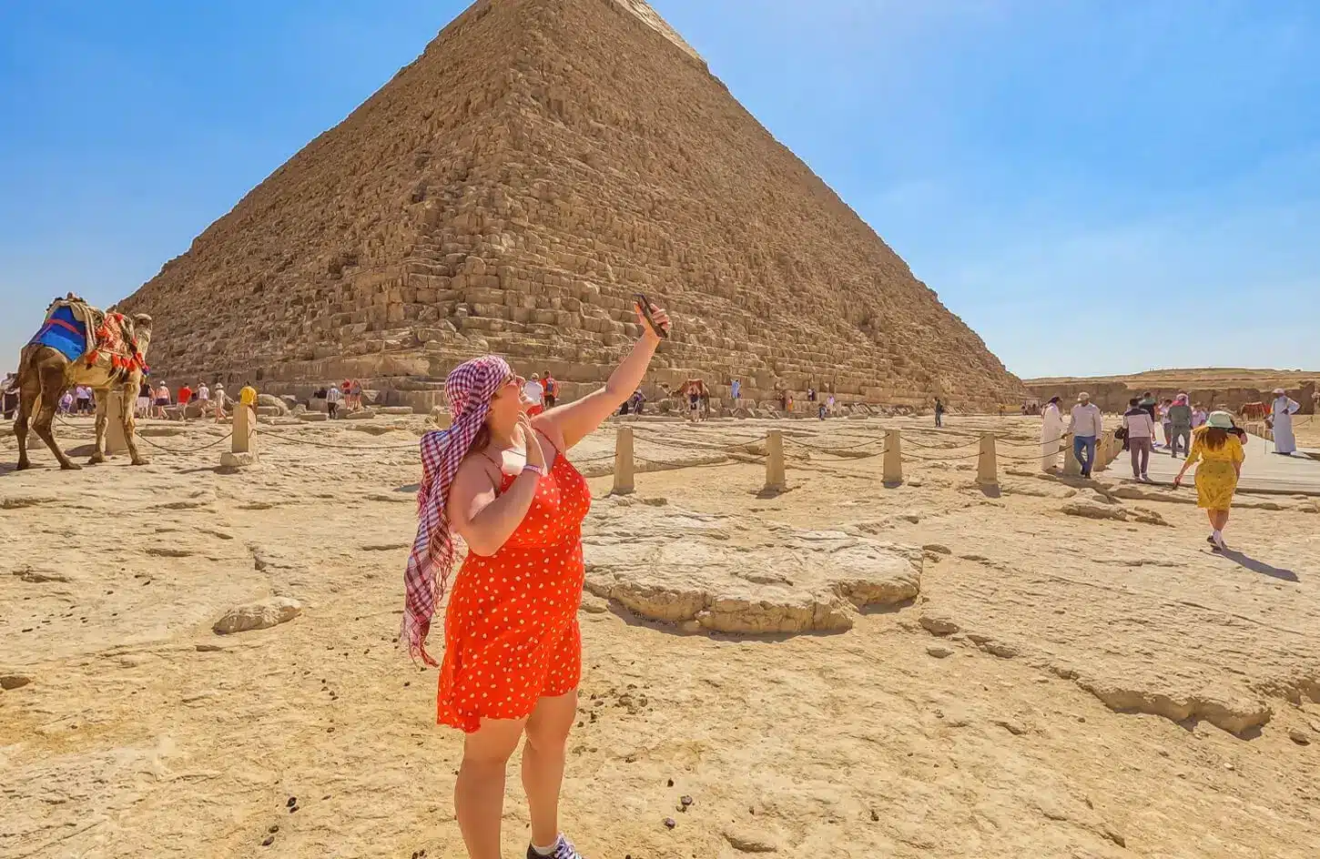 Woman in red dress taking a selfie at the Giza Pyramids Egypt during a sunny desert tour