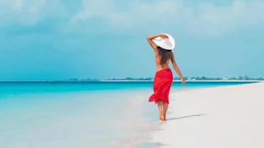 A woman in a red sarong walking on a white sand beach in Egypt during a luxury summer vacation.