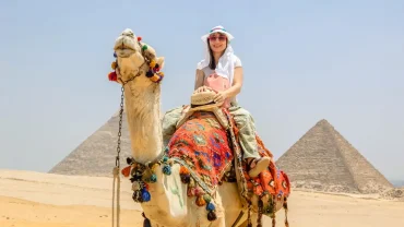 Tourist riding a camel at the Giza Pyramid Complex in Egypt with the Great Pyramids in the background