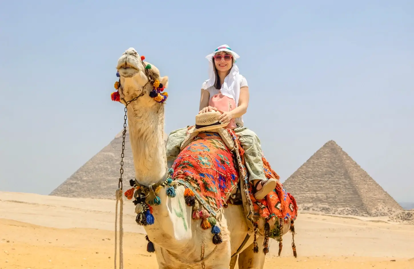 Tourist riding a camel at the Giza Pyramid Complex in Egypt with the Great Pyramids in the background