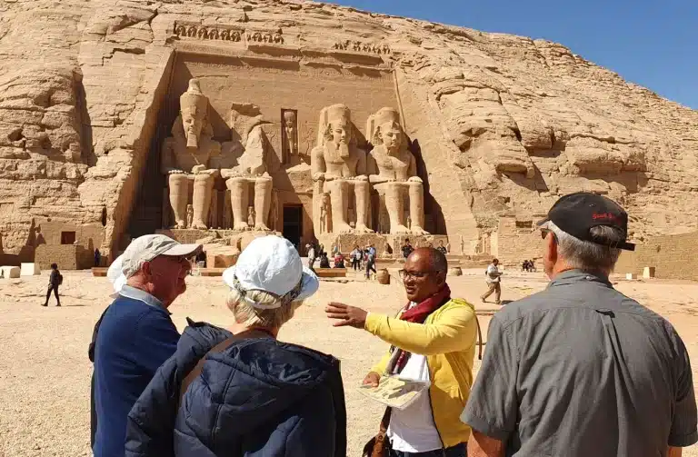 Tour guide in Egypt explaining the history of Abu Simbel Temple to tourists in front of the Ramses II statues.
