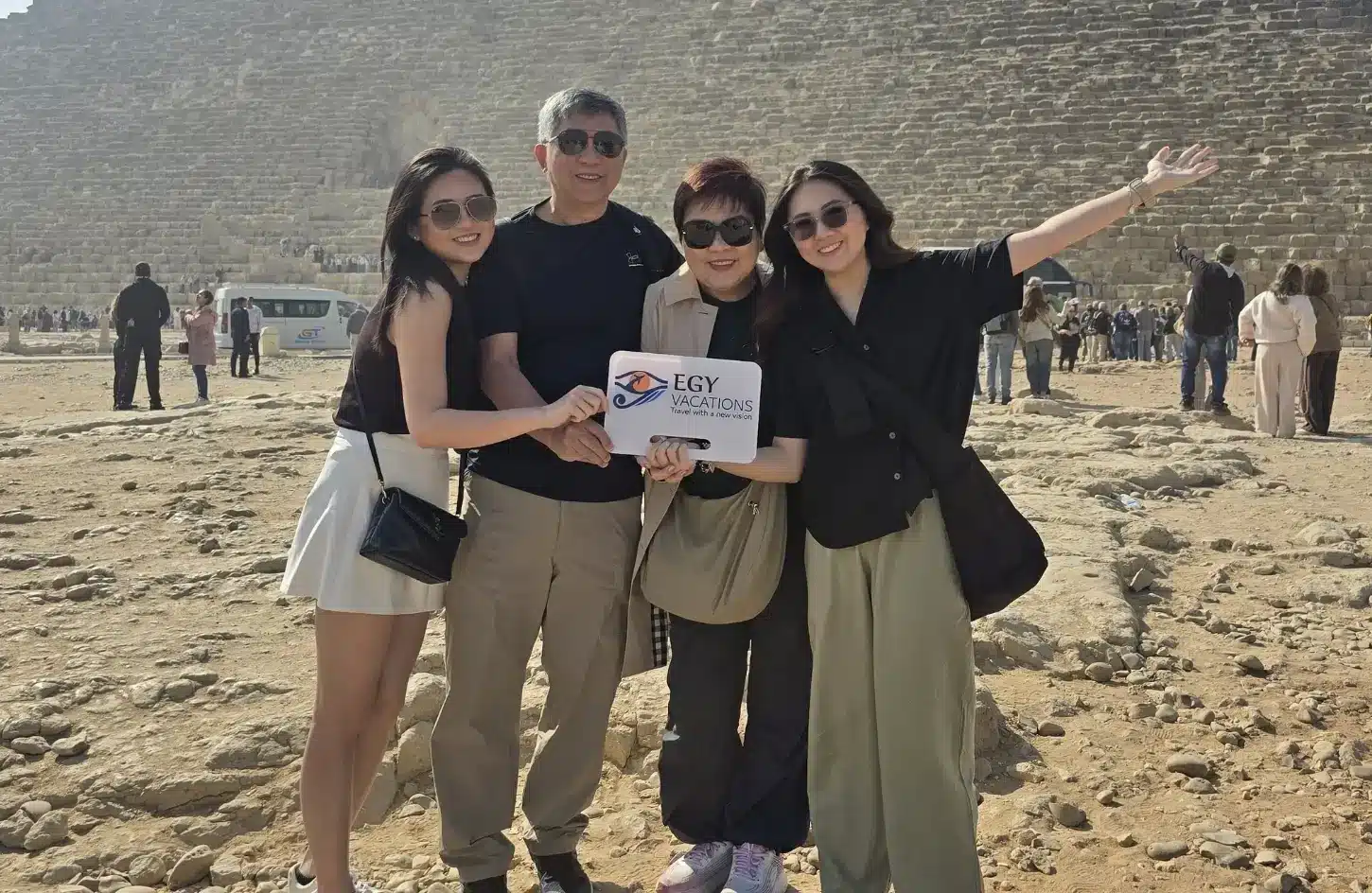 A family on a guided tour in Egypt posing with an Egy Vacations sign at the Great Pyramid of Giza.